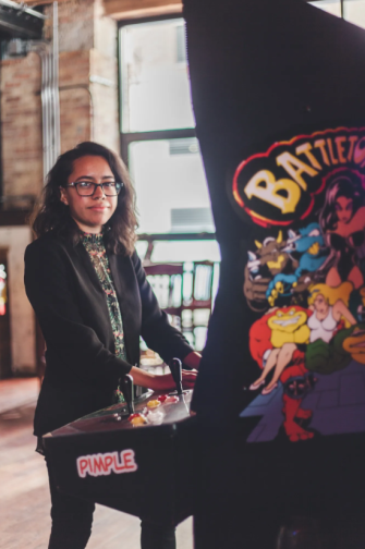 Janet Garcia standing at a Battletoads arcade, looking at the camera. Photo credit Ally Almore.
